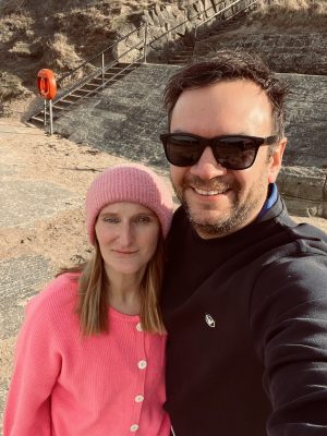 Laura standing with her partner on a beach after recovering from acoustic neuroma surgery